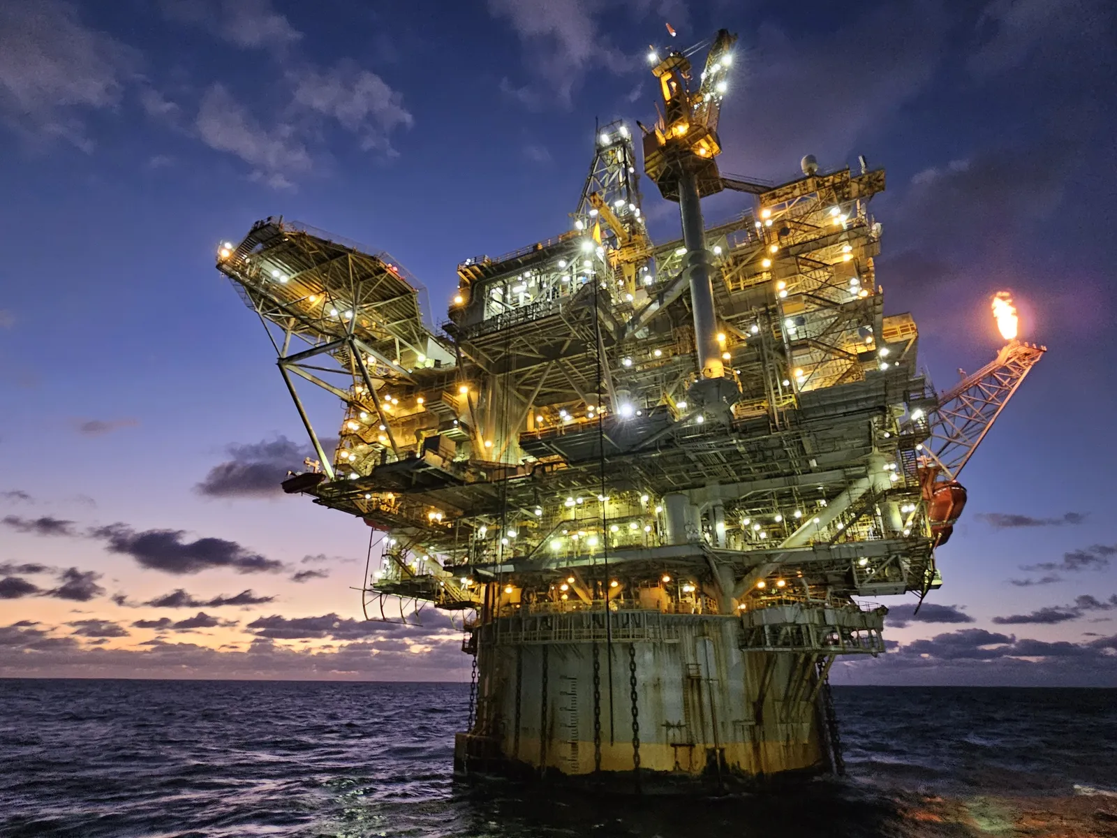 Plataforma de produção de petróleo iluminada ao entardecer.